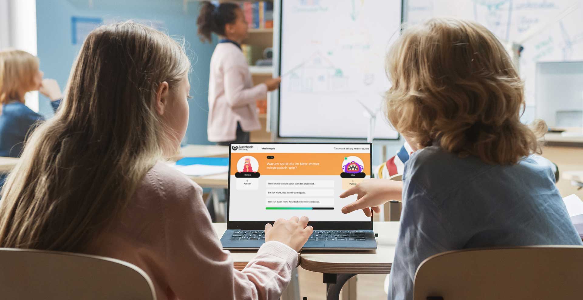 Zwei Kinder schauen auf einen Computerbildschirm mit der geöffneten Medienquiz-Seite.