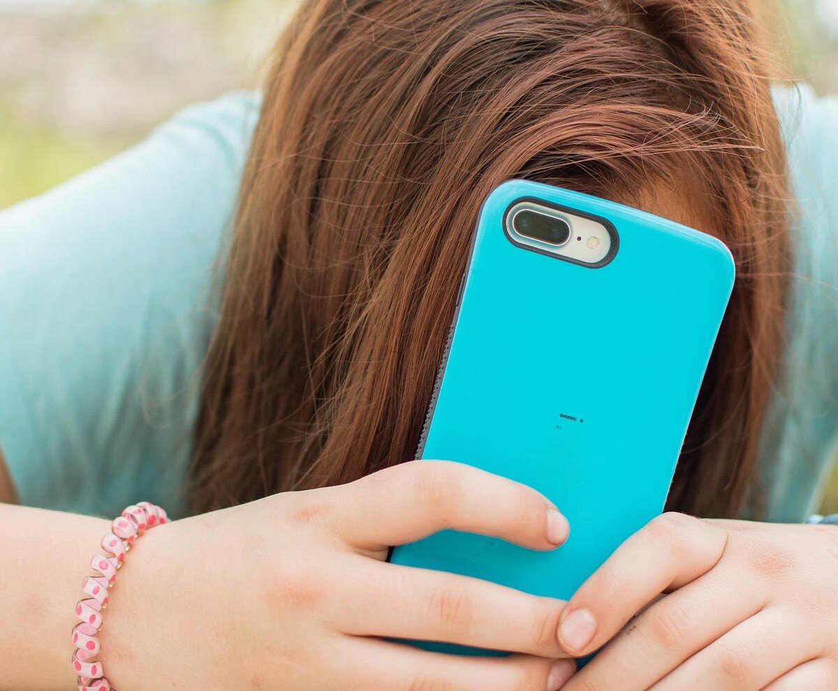 Trauriges Mädchen mit Smartphone in der Hand und dem Kopf auf dem Tisch