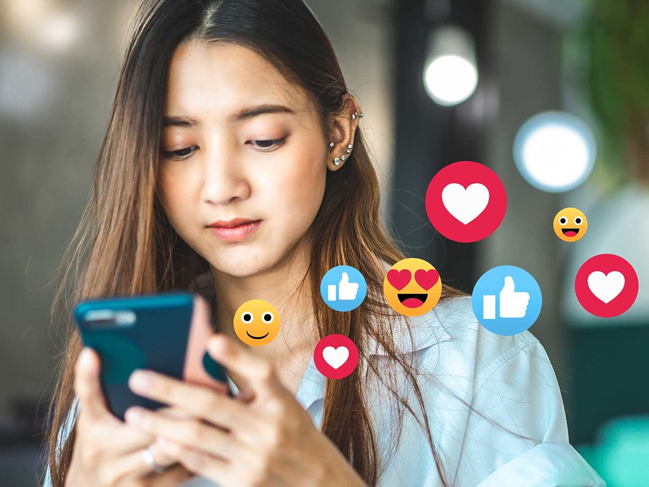 Ein Mädchen schaut auf ihr Handy, während verschiedene Symbole und Emojis aus dem Handy schweben.