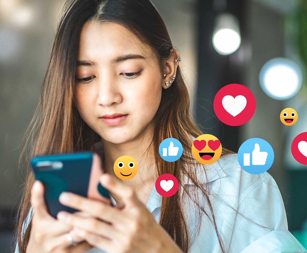 Ein Mädchen schaut auf ihr Handy, während verschiedene Symbole und Emojis aus dem Handy schweben.