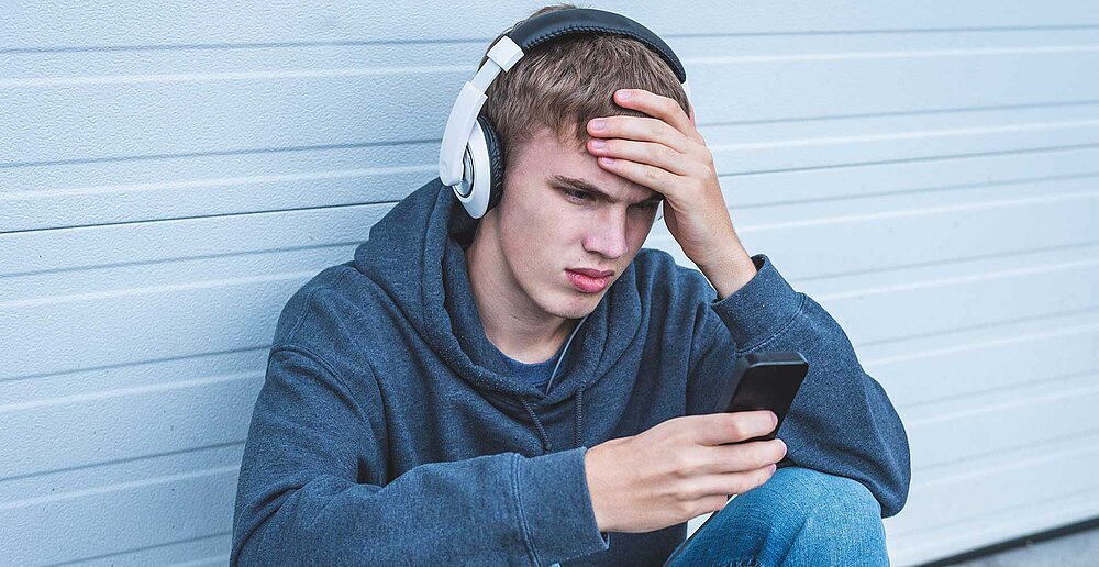 Teenager schaut traurig in sein Handy