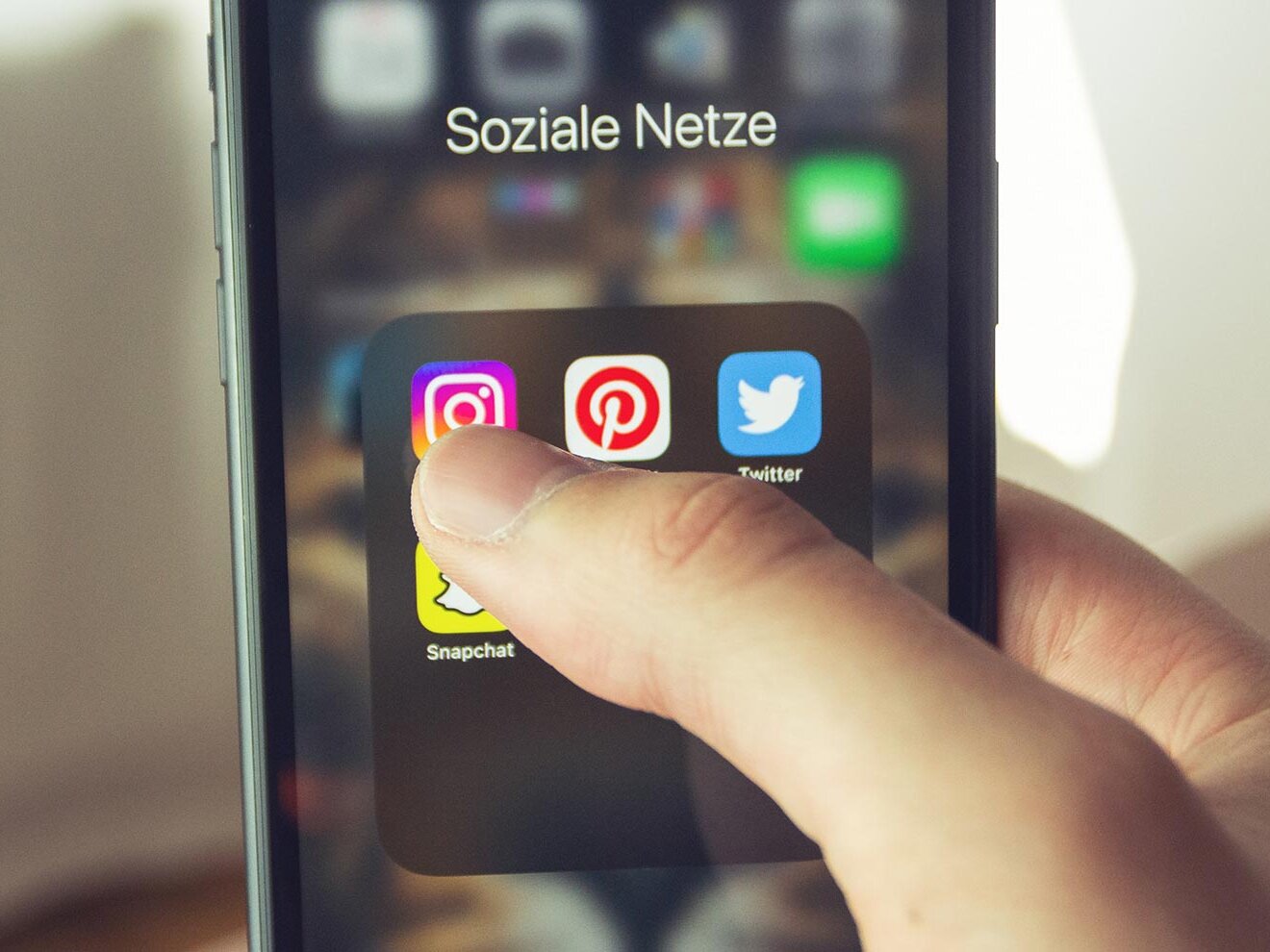 Hand hält ein Smartphone, darauf sind verschiedene App-Icons von sozialen Netzwerken abgebildet.