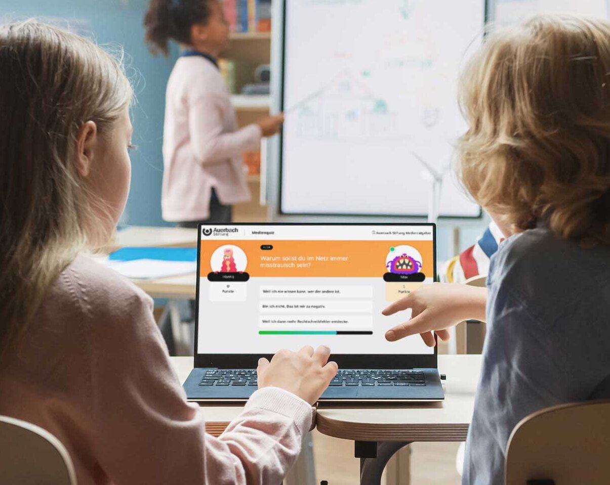 Zwei Kinder schauen auf einen Computerbildschirm mit der geöffneten Medienquiz-Seite.