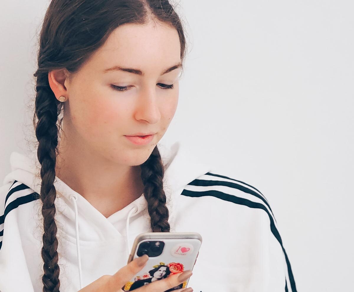 Ein junges Mädchen mit Zöpfen blickt angeregt auf ein Handy