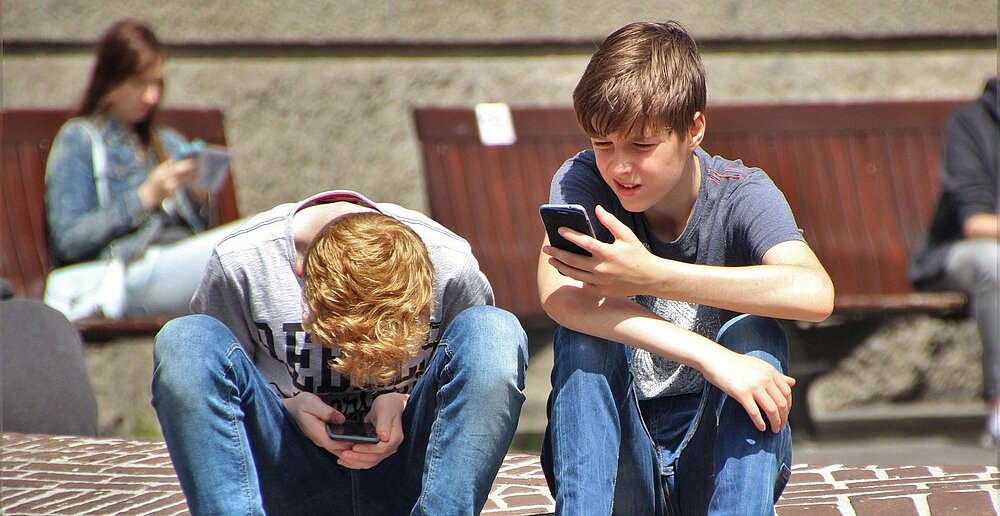 Zwei Jungen sitzen im Freien und schauen auf ihr Handy