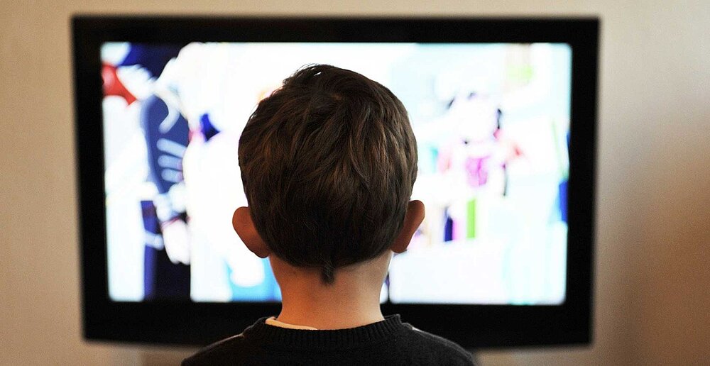 Ein kleiner Junge sitzt frontal vor einem Fernseher