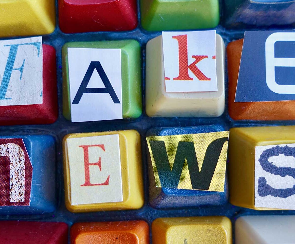 Auf einer bunt angemalten Computertastatur ist der Begriff "Fake News" aufgeklebt.