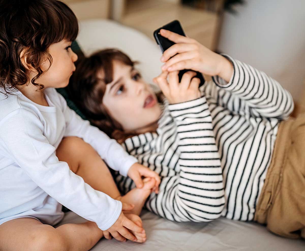 Ein Junge liegt mit seinem kleinen Bruder auf einem Sofa und schaut in sein Handy