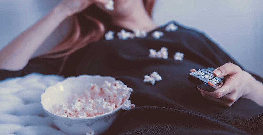 Ein Mädchen schaut fern und isst nebenher Popcorn