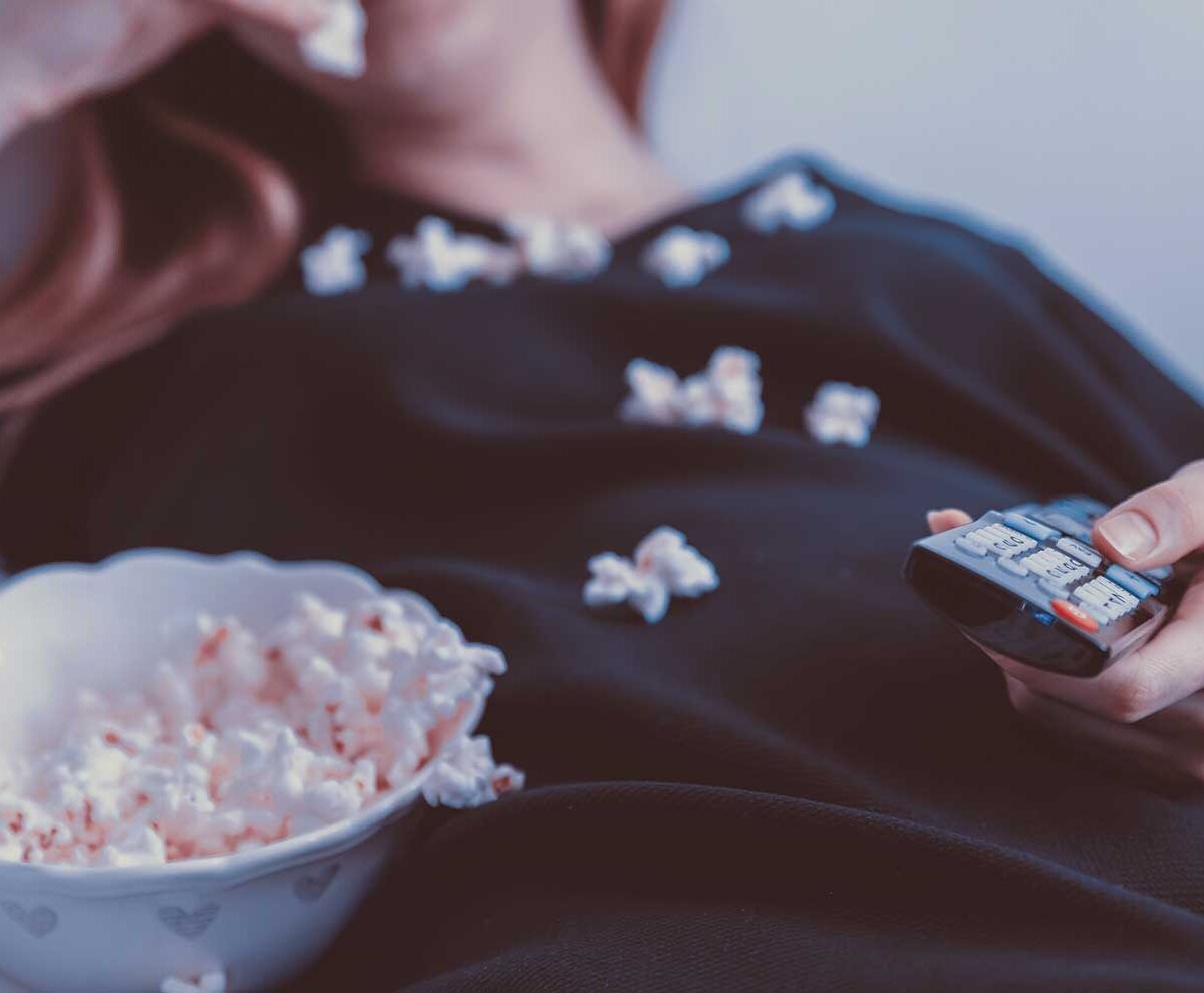 Ein Mädchen schaut fern und isst nebenher Popcorn