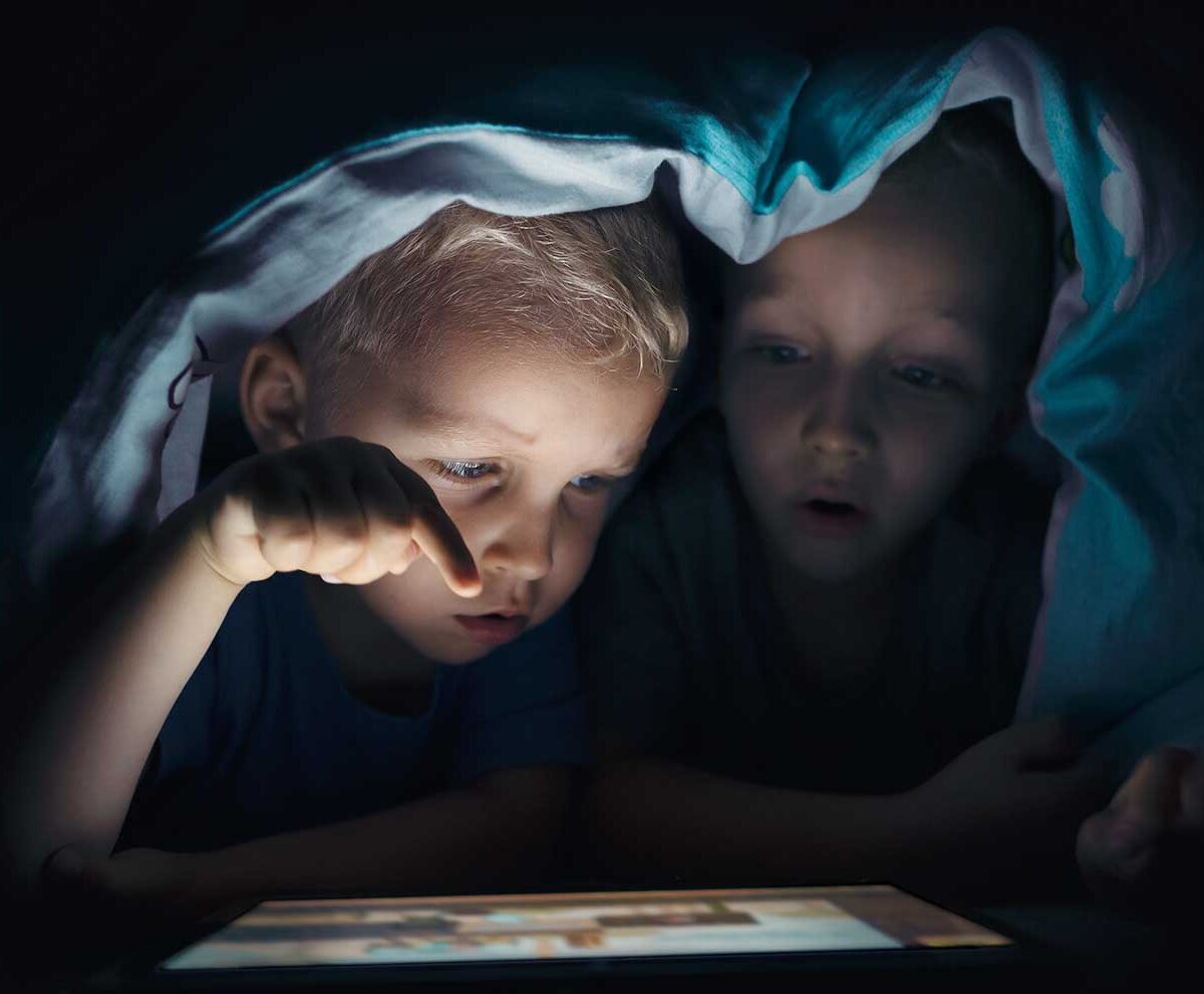 Zwei Geschwister spielen unter einer Bettdecke heimlich Computerspiele.