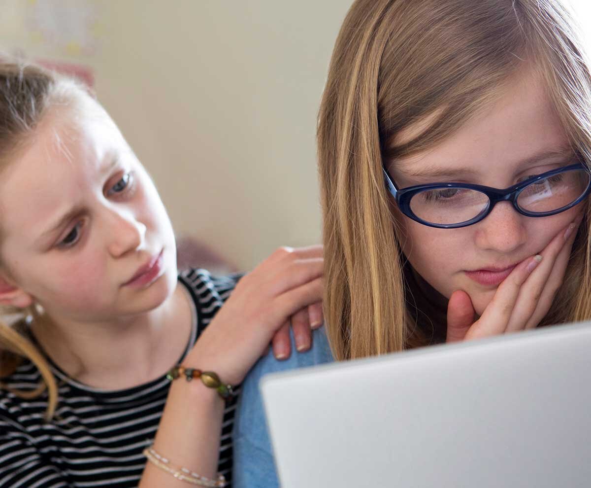 Ein Mädchen sitzt verzweilfelt vor einem Laptop und wird von einer Freundin getröstet.