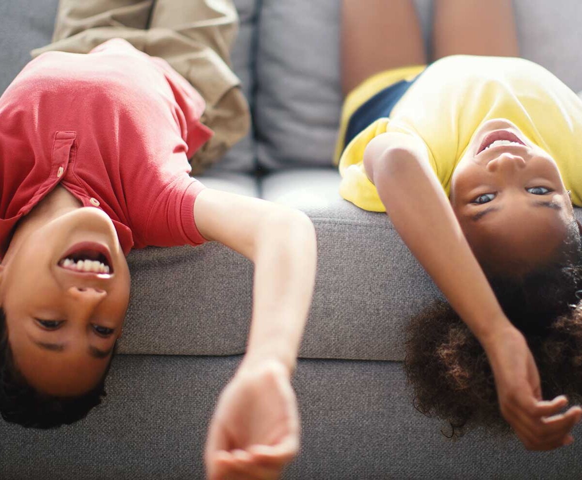 Ein Mädchen und ein Junge liegen kopfüber auf einer Couch.